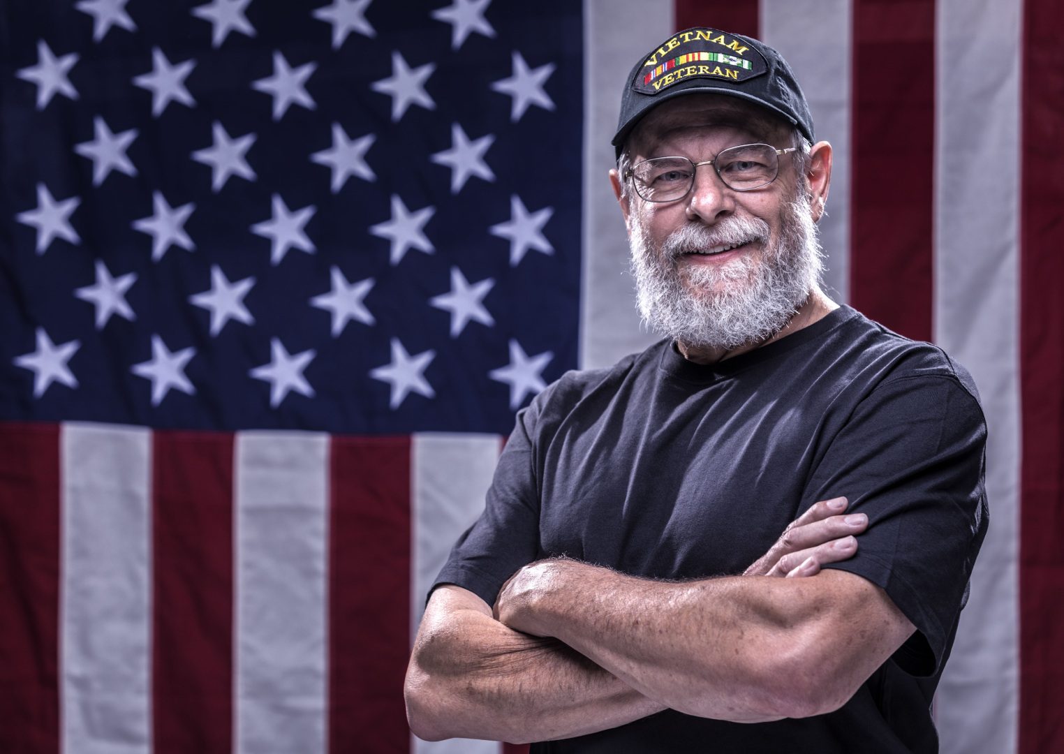 A man with beard and hat standing in front of an american flag.